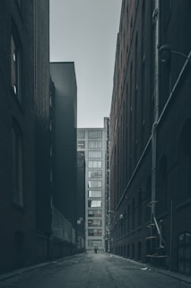 man walking in the middle of city buildings under gray clouds