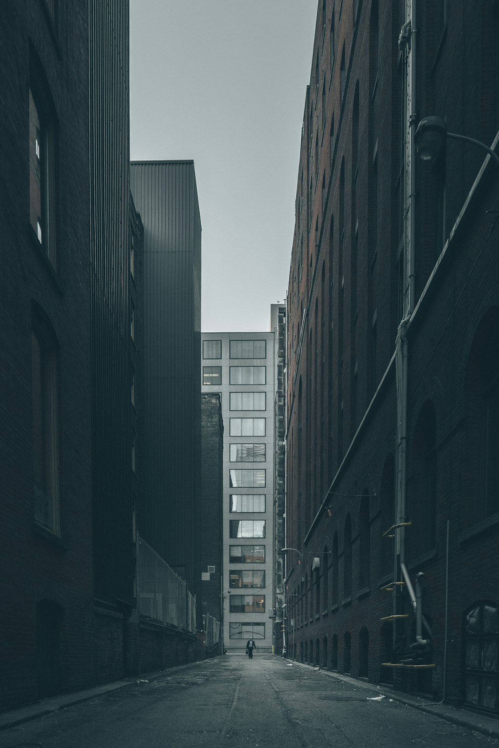 회색 구름 아래 도시 건물 한가운데를 걷는 남자