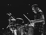 Close-up of drummer’s fierce expression mid-beat, sweat glistening in dim lighting.