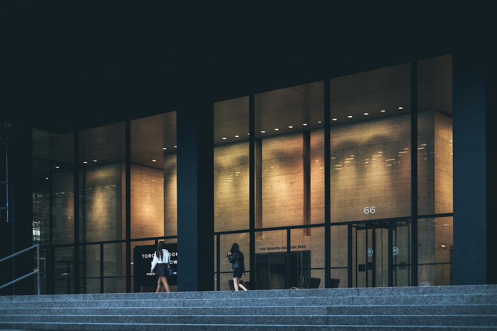 two woman walking near clear glass wall