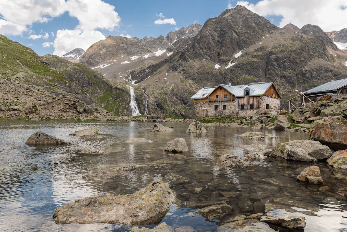 Cabaña de madera junto al agua, rodeada de bosque y montañas