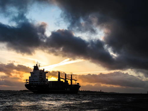 A sleek cargo ship silhouetted against a deep blue twilight sky at sea.
