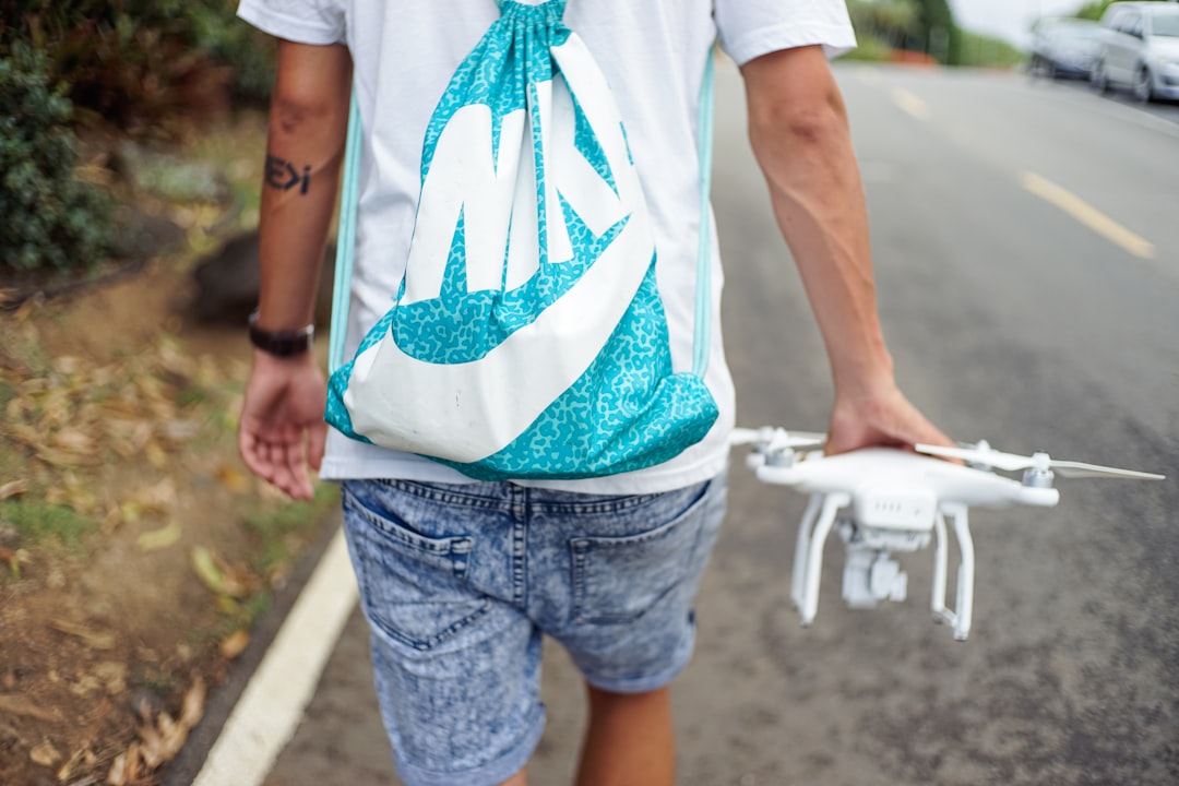 man holding white R/C quadcopter while walking beside concrete roadway