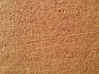 A close-up view of a textured cork board surface, displaying a pattern of tightly packed, irregular cork granules with a rough texture.