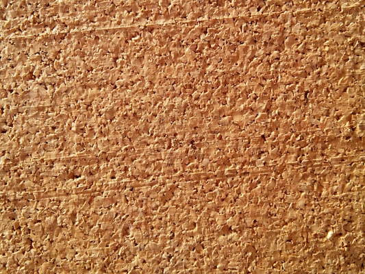A close-up view of a cork board, characterized by its rough, textured surface and natural brown tones. The image highlights the irregular patterns and grain structure of the cork material.