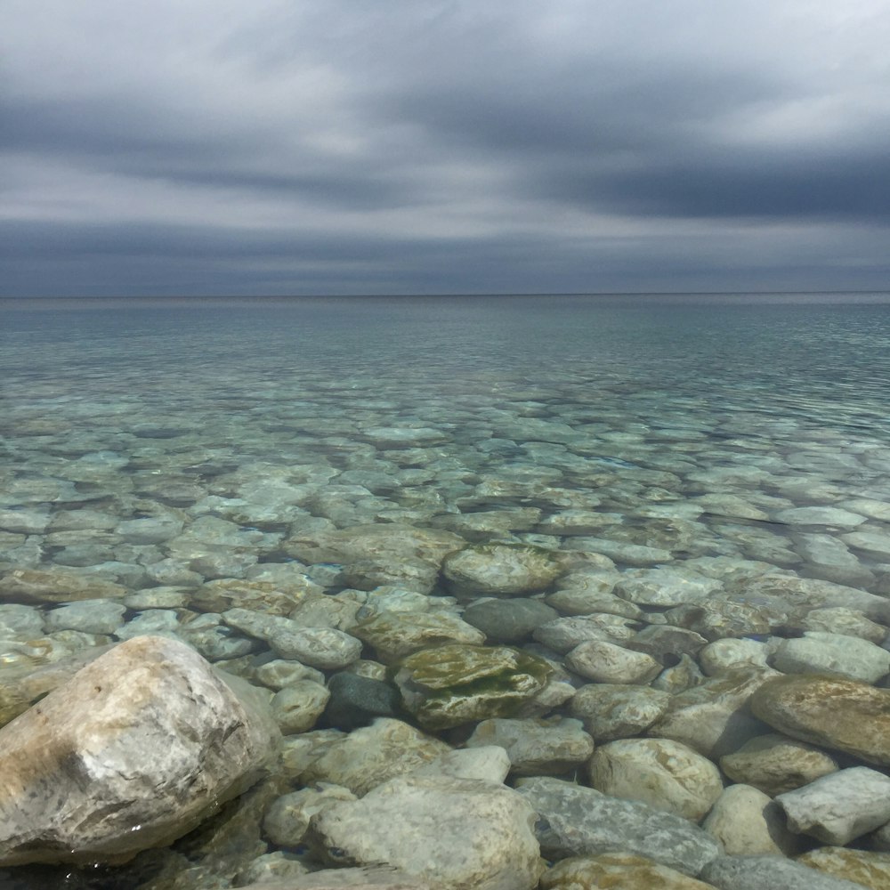 body of water with stones under cloudy sky