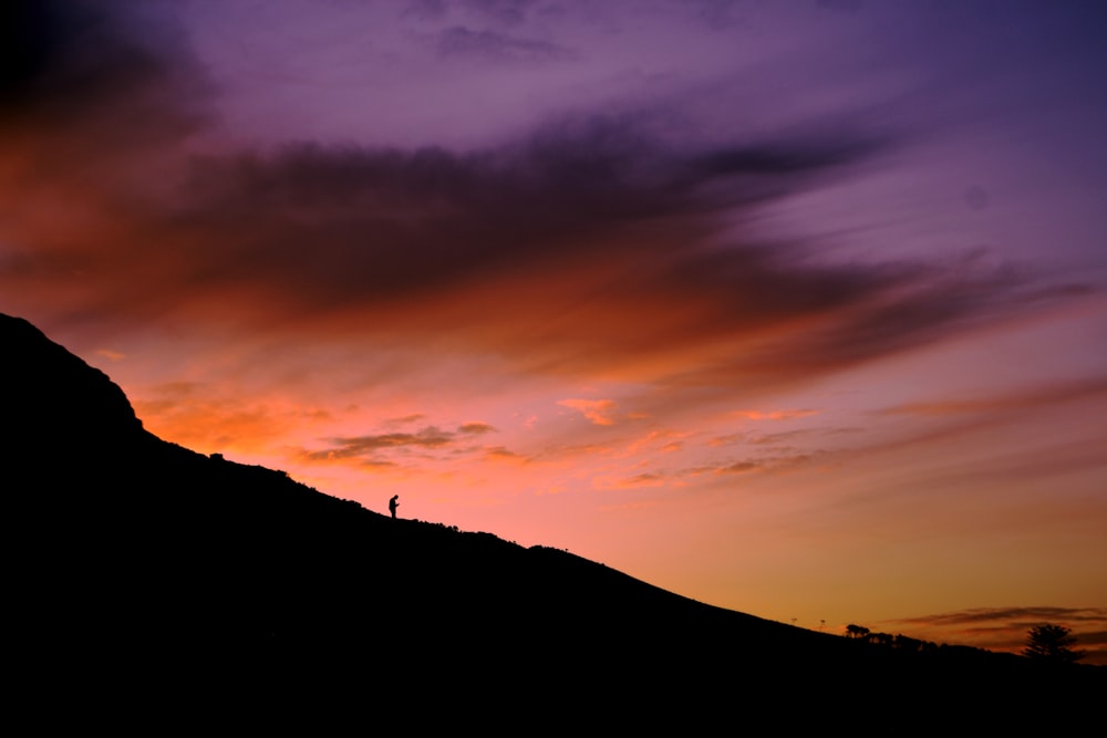 une personne debout au sommet d’une colline au coucher du soleil