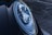 Close-up of a car's headlight featuring a sleek, modern design with intricate reflective components. The surface of the headlight showcases sharp lines and a glossy finish. The surrounding body of the car is dark and polished, contributing to a luxurious vibe.