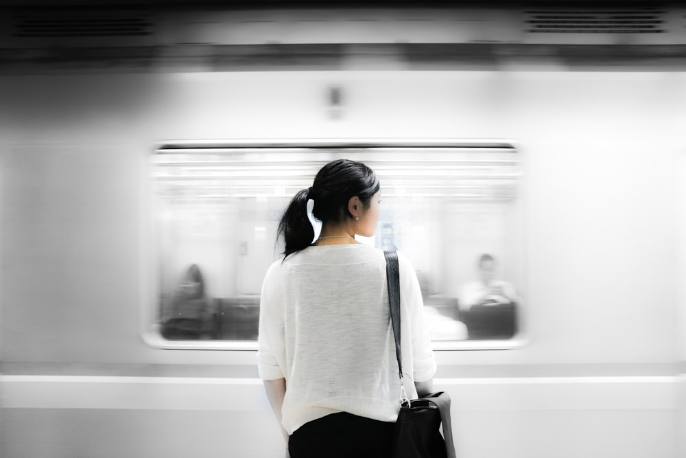 地下鉄の白い電車のそばに立つ白い肘袖のシャツを着た女性