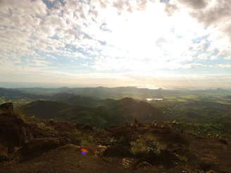 Panoramic view from a summit showing rolling hills and distant peaks bathed in golden afternoon light