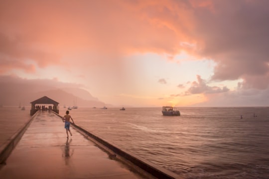 boy running on dock under cloudy sky in Hanalei Bay United States