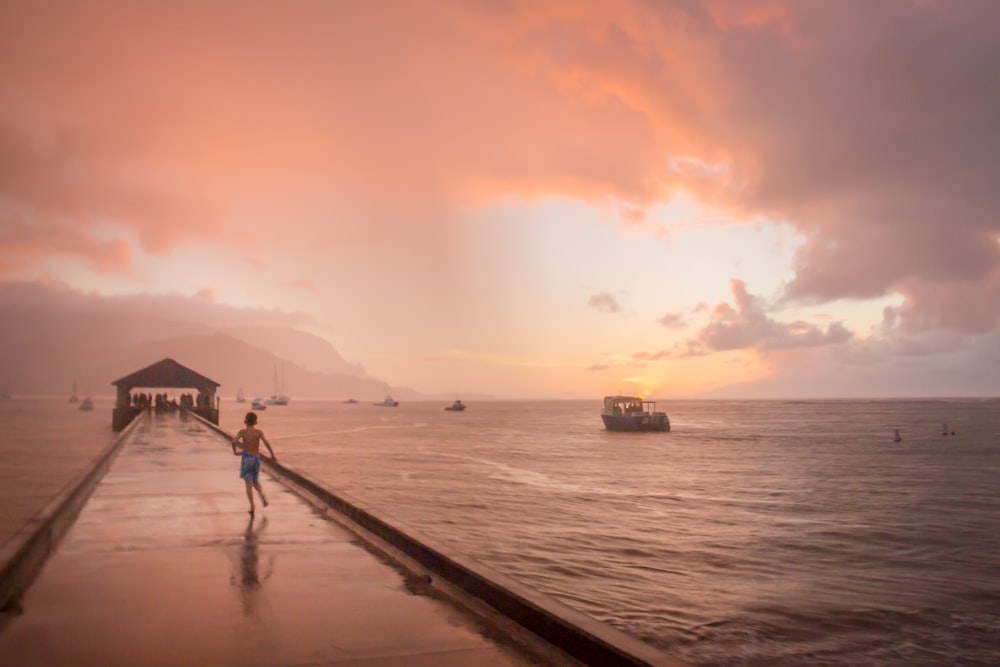 boy running on dock under cloudy sky