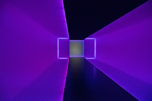 A futuristic tunnel with glowing purple walls converges into a bright white light at the far end. Symmetrical and geometric in design, creating a visually stunning and immersive experience.