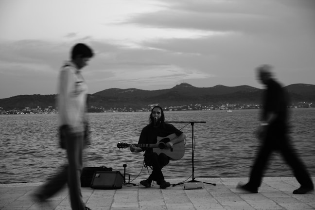 A candid moment of a street musician playing guitar on a rainy day in a Northern town.