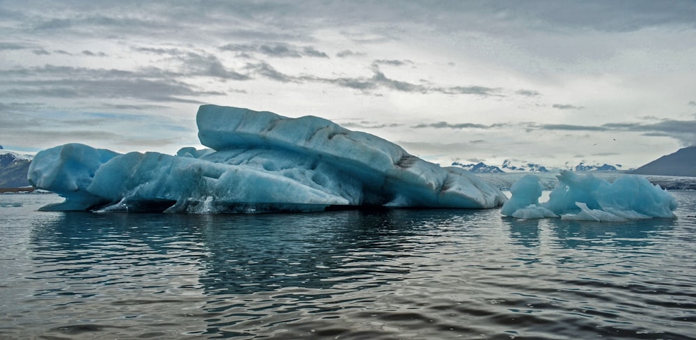 body of water with iceberg under cloudy sky