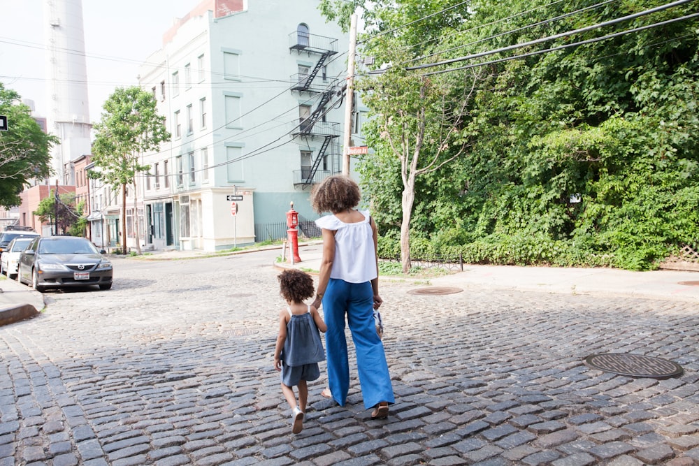 woman in white cap-sleeved shirt and blue pants walking beside girl in gray tank top