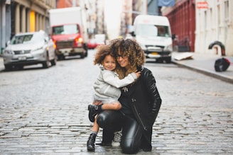 photography of woman carrying baby near street during daytime
