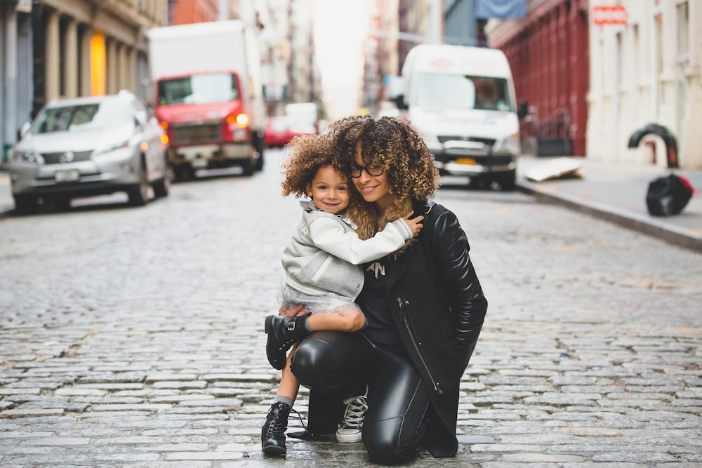 fotografia da mulher que carrega o bebê perto da rua durante o dia