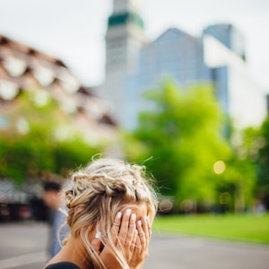 person covering face with hands outdoors