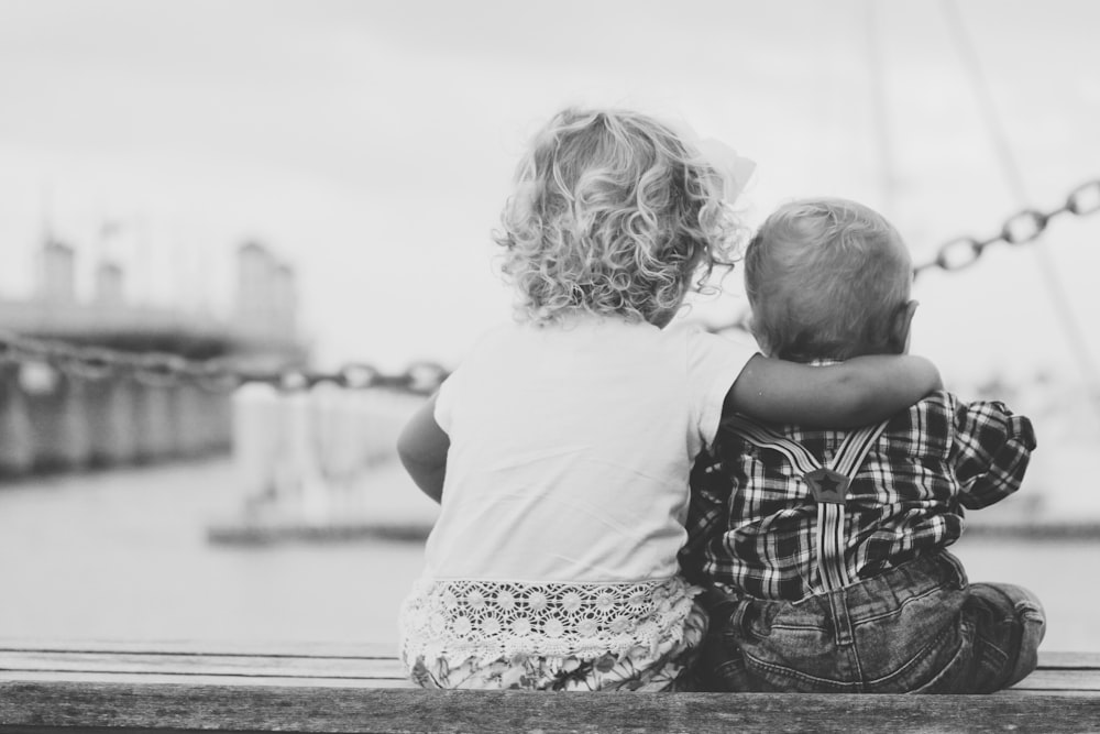 grayscale photography of two children sitting on ledge