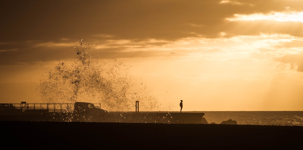 silhouette photo of human standing on beach shore during orange sunset