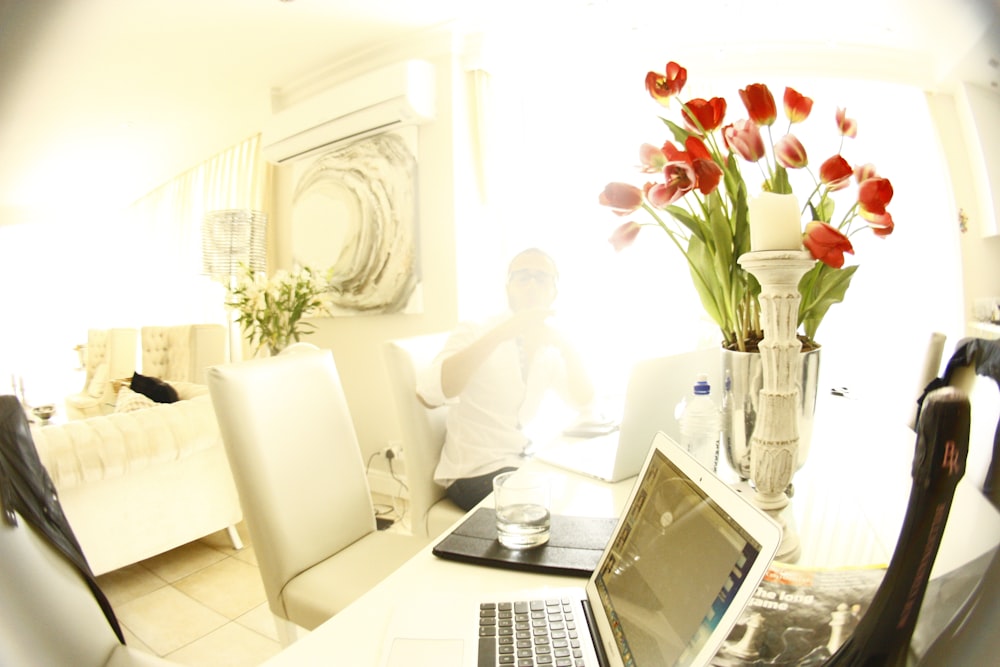 A laptop next to a vase full of red roses.