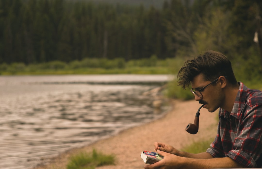 man smoking on pipe beside lake