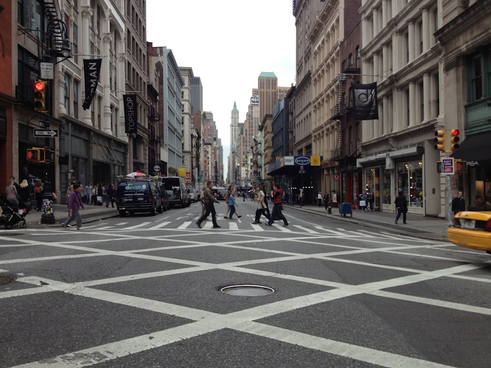 people walking on black and white concrete road between high buildings under white sky during daytime