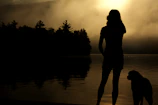 A serene early morning scene with mist over the water and a person with their dog ready to start cani paddle.