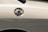 A close-up view of a car's fuel cap on the side of a light-colored vehicle. The metal cap is shiny and reflective, with the word 'FUEL' clearly marked on top.