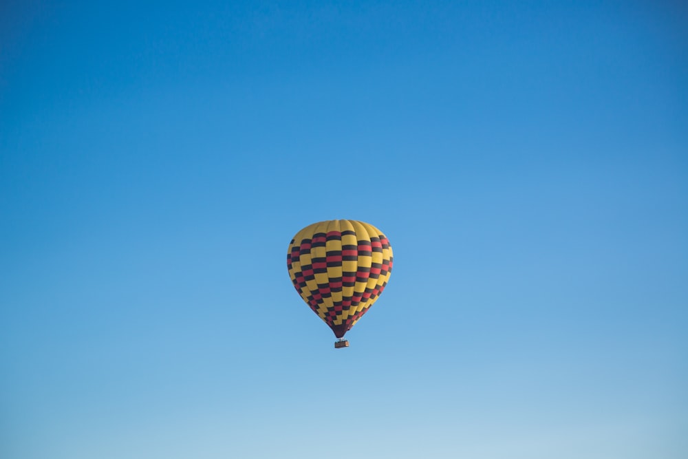 globo aerostático amarillo y rosa flotando bajo el cielo azul durante el día