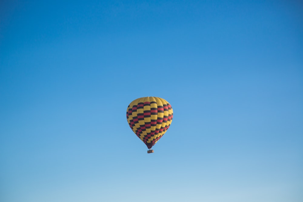 Montgolfière jaune et rose flottant sous le ciel bleu pendant la journée