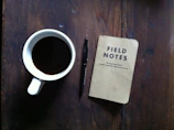 A minimalist desk with a journal, pen, and a cup of black coffee under soft lighting.