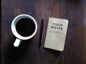 Overhead shot of a coffee table with a 'Boss That Brew' mug, a notebook filled with hustle plans, and a gold pen