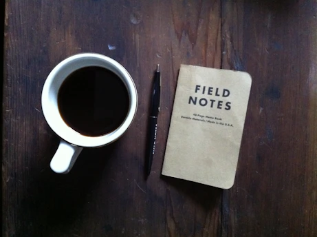A cozy workspace with a notebook, pen, and a cup of coffee on a wooden table.