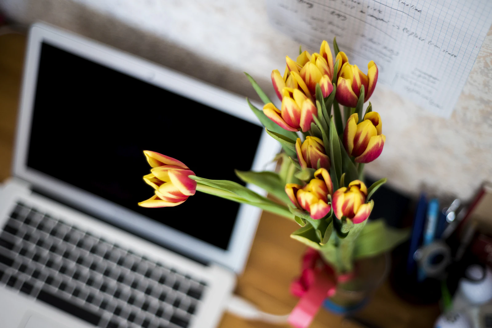 Silver laptop on a desk beside a vase of tulips
