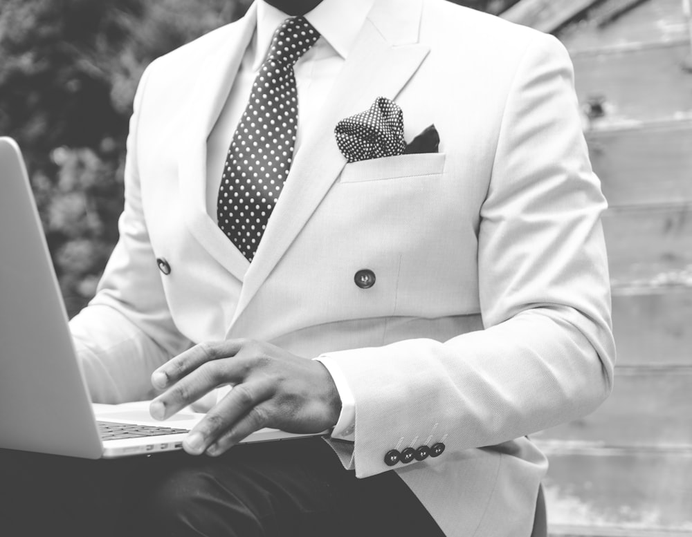 grayscale photo of man wearing suit jacket using laptop