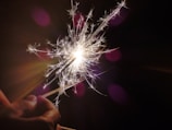 A hand holds a sparker emitting bright, fiery sparks against a dark background, creating a striking contrast and highlighting the intricate details of the sparks.