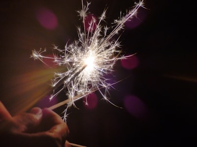 A hand holds a sparker emitting bright, fiery sparks against a dark background, creating a striking contrast and highlighting the intricate details of the sparks.
