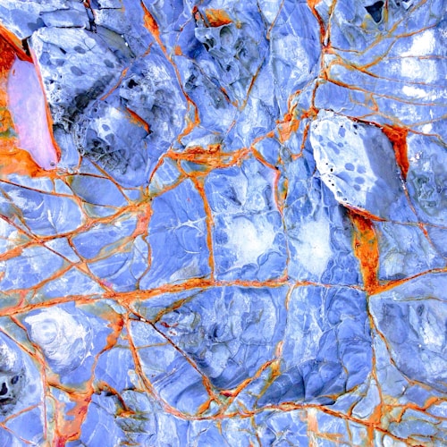 An abstract pattern resembles a cracked surface with vibrant blue and orange hues. The irregular lines and color contrasts suggest a natural rock formation or artistic rendering.