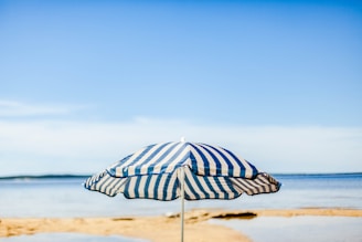 A beach umbrella with bold stripes planted firmly in the sand, waves gently rolling in the background.
