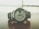 A sleek silver wristwatch rests on a wooden surface. The watch face displays the time with large numerals and features a day-date window. The metal bracelet complements the overall modern and sophisticated design, while the background appears blurred, emphasizing the watch.