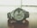 A sleek silver wristwatch rests on a wooden surface. The watch face displays the time with large numerals and features a day-date window. The metal bracelet complements the overall modern and sophisticated design, while the background appears blurred, emphasizing the watch.