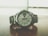 A sleek silver wristwatch rests on a wooden surface. The watch face displays the time with large numerals and features a day-date window. The metal bracelet complements the overall modern and sophisticated design, while the background appears blurred, emphasizing the watch.