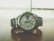 A sleek silver wristwatch rests on a wooden surface. The watch face displays the time with large numerals and features a day-date window. The metal bracelet complements the overall modern and sophisticated design, while the background appears blurred, emphasizing the watch.
