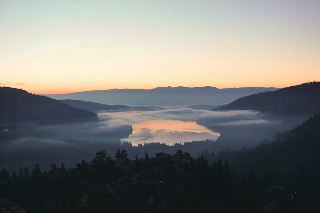 A serene sunrise over a misty Patagonian lake surrounded by towering mountains.