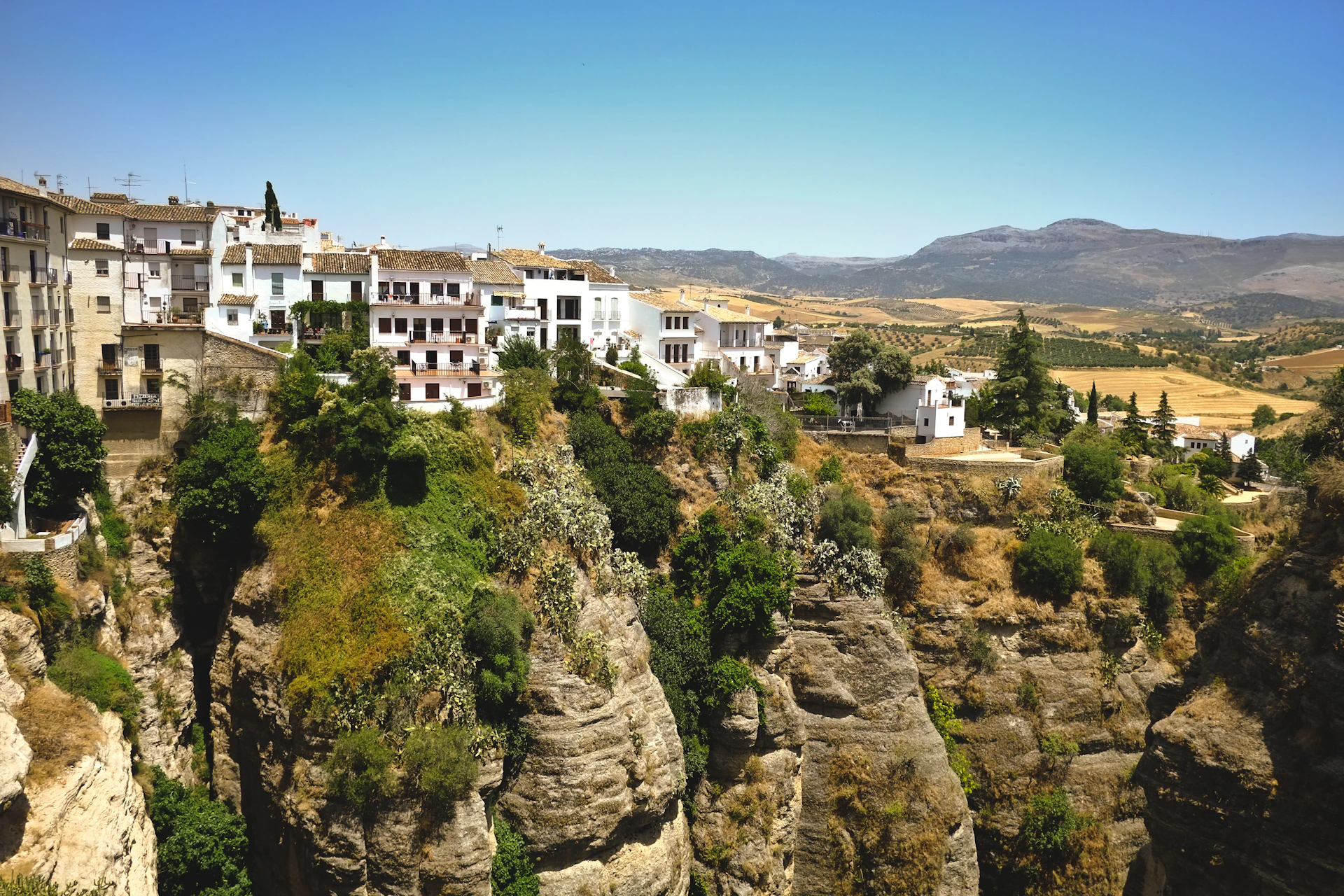 A breathtaking aerial view of the whitewashed village of Mijas nestled against rolling olive-covered hills under a clear blue sky.