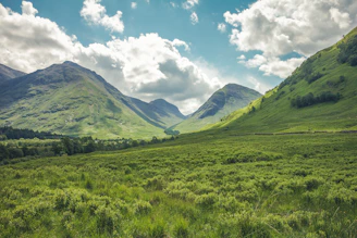 A green valley between mountains under a blue sky with white clouds in Scotland