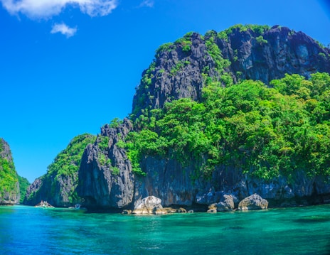 body of water beside mountain and trees under blue and white sky at daytime