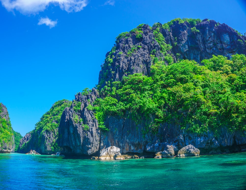 body of water beside mountain and trees under blue and white sky at daytime